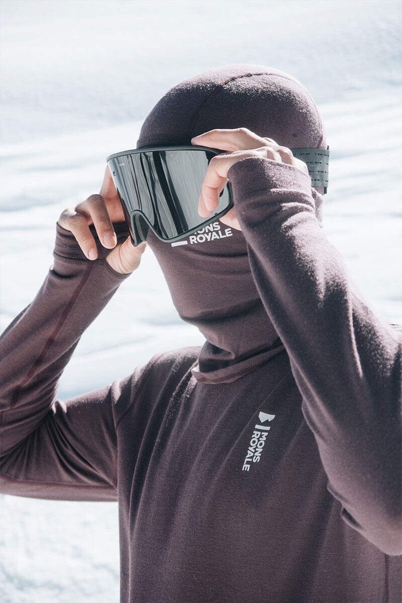 Man wears head to toe Merino thermal layers and balaclava in the snow, re-adjusting his snow goggles